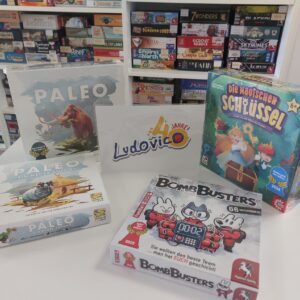 Ein Tisch mit den Spielen Die magischen Schlüssel, Bom Busters und Paleo samt der Erweiterung Eine neuer Anfang. Dazu ein Schild mit der Aufschrift "Ludovico 40 Jahre".